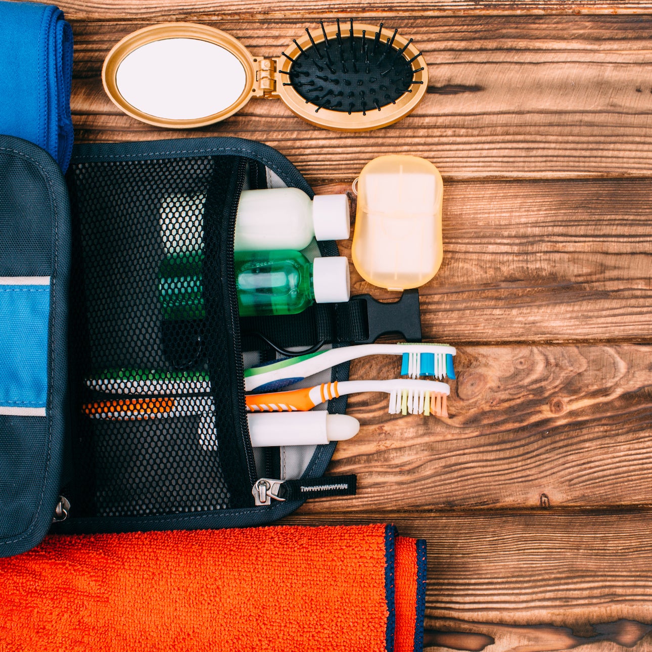 Top view of kit for hygiene during hiking and travel on wooden table with empty space. Items include towel, comb, soap, toothbrushes, shampoo