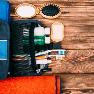 Top view of kit for hygiene during hiking and travel on wooden table with empty space. Items include towel, comb, soap, toothbrushes, shampoo