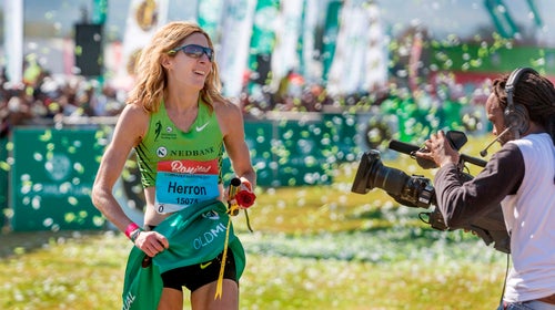 Camille Herron is crossing the finish line, dressed in green, with confetti everywhere.