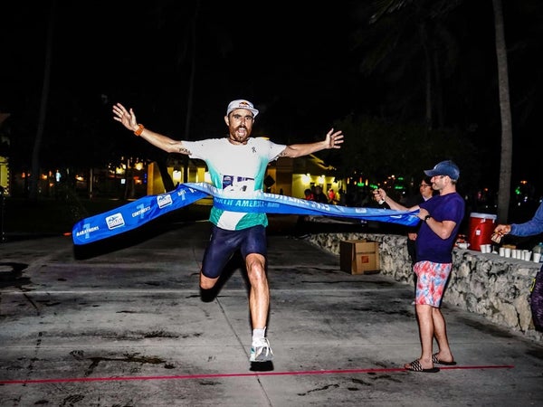 A man crosses a finish line that is blue to a crowd at night