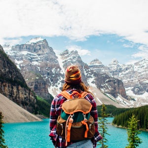 A woman wearing a backpack looking out towards a blue lake with large mountains in the background