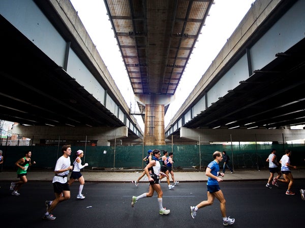 several runners of the NYC marathon run left to right under a shadowy tunnel