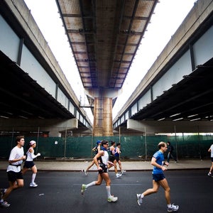 several runners of the NYC marathon run left to right under a shadowy tunnel