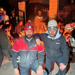 Polat Dede, on the left, and Olcay Tepe, on the right, pose for a photo outside a closed cafe in Antakya, Turkey, during the earthquake relief efforts. Behind them is a group of group of coal miners from the town of Zonguldak who were also volunteering.
