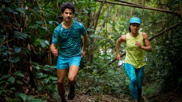 Two runners in colorful clothes run in a green forest