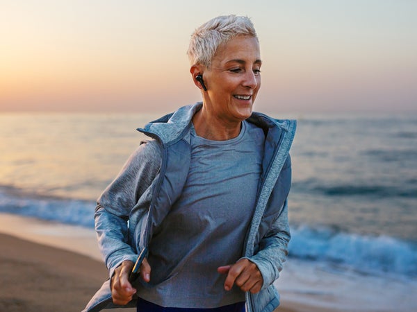 mature runner smiling and jogging on shore near waving sea at sunset