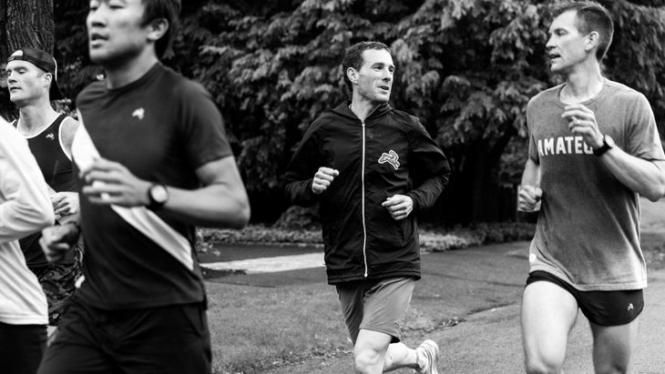 A group of men run along the a road and it is black and white