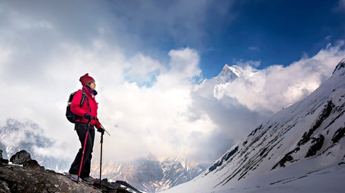 A hiker with trekking poles stands among the snowy Himalayan mountains.