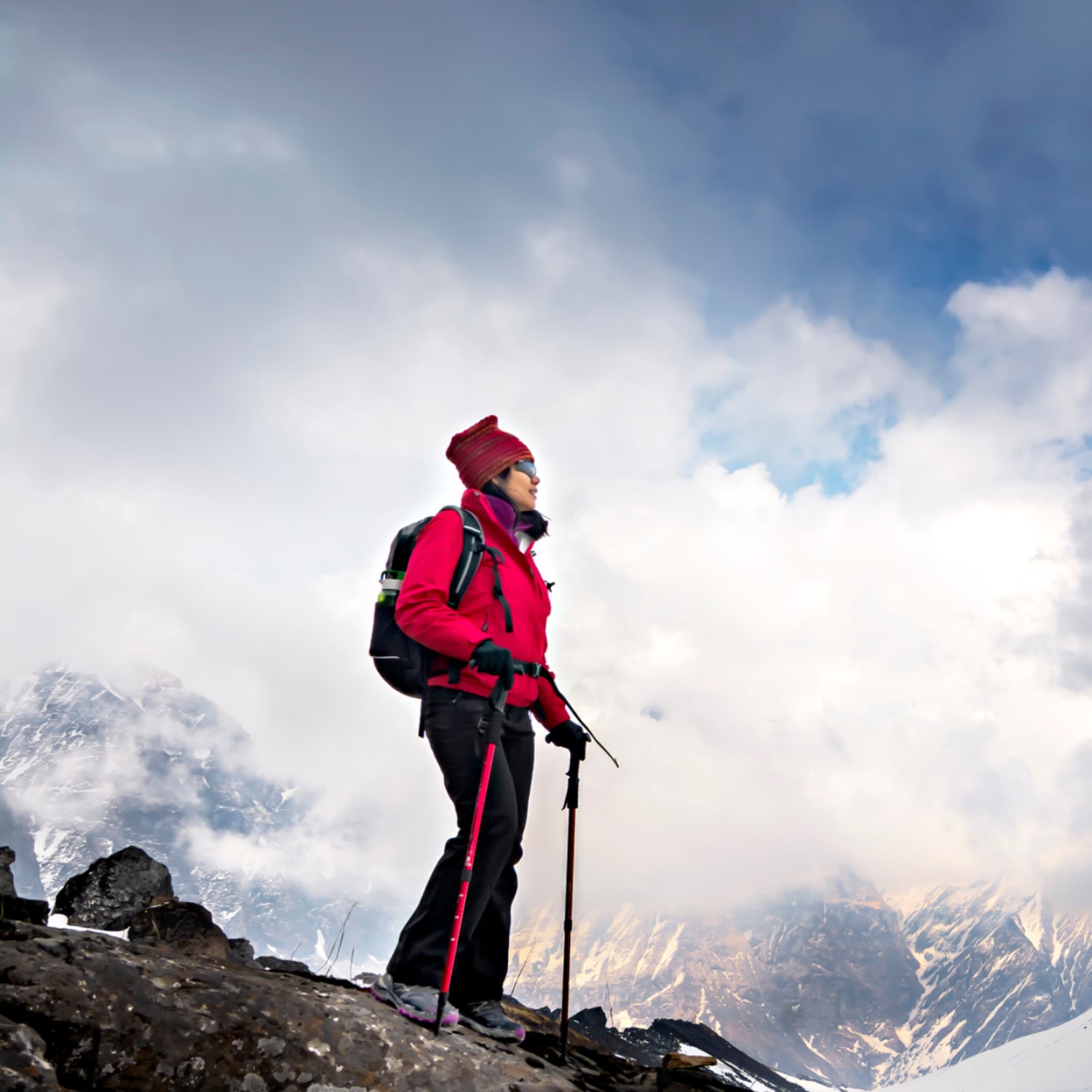 A hiker with trekking poles stands among the snowy Himalayan mountains.