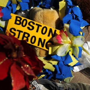 A yellow sign that says Boston Strong surrounded by yellow and blue flowers
