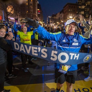 Dave McGillivray runs through a blue finish line tape surrounded by a large crowd