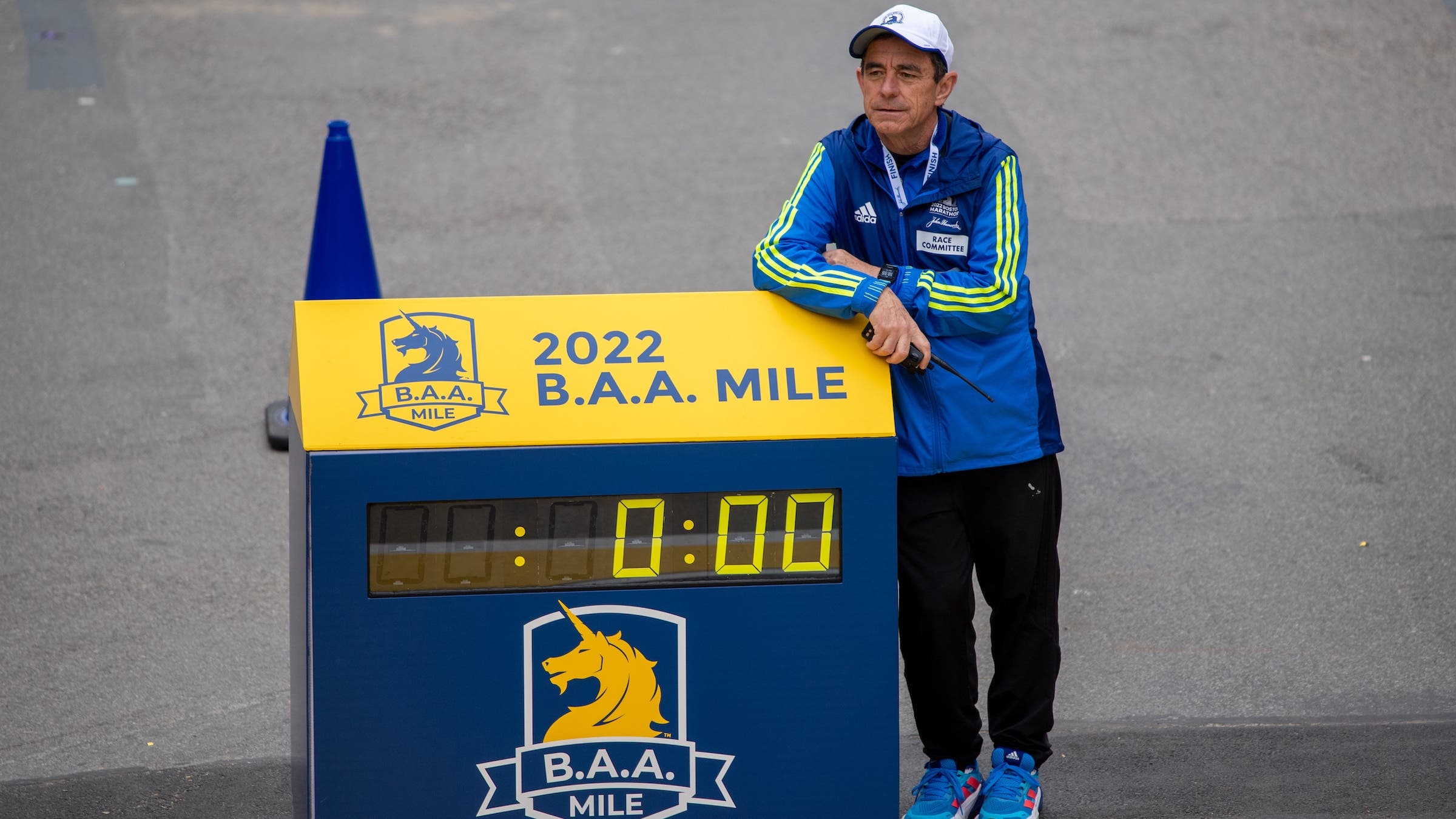 A man in blue leans on a Boston Marathon sign with a walkie talkie
