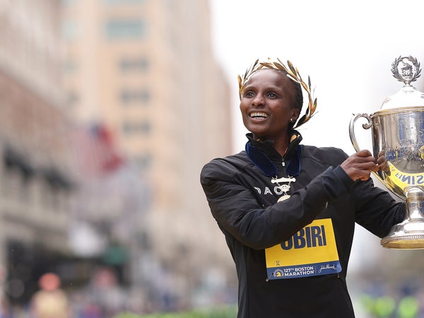 Obiri holds up a trophy with laurels on her head at the finish line of the boston marathon