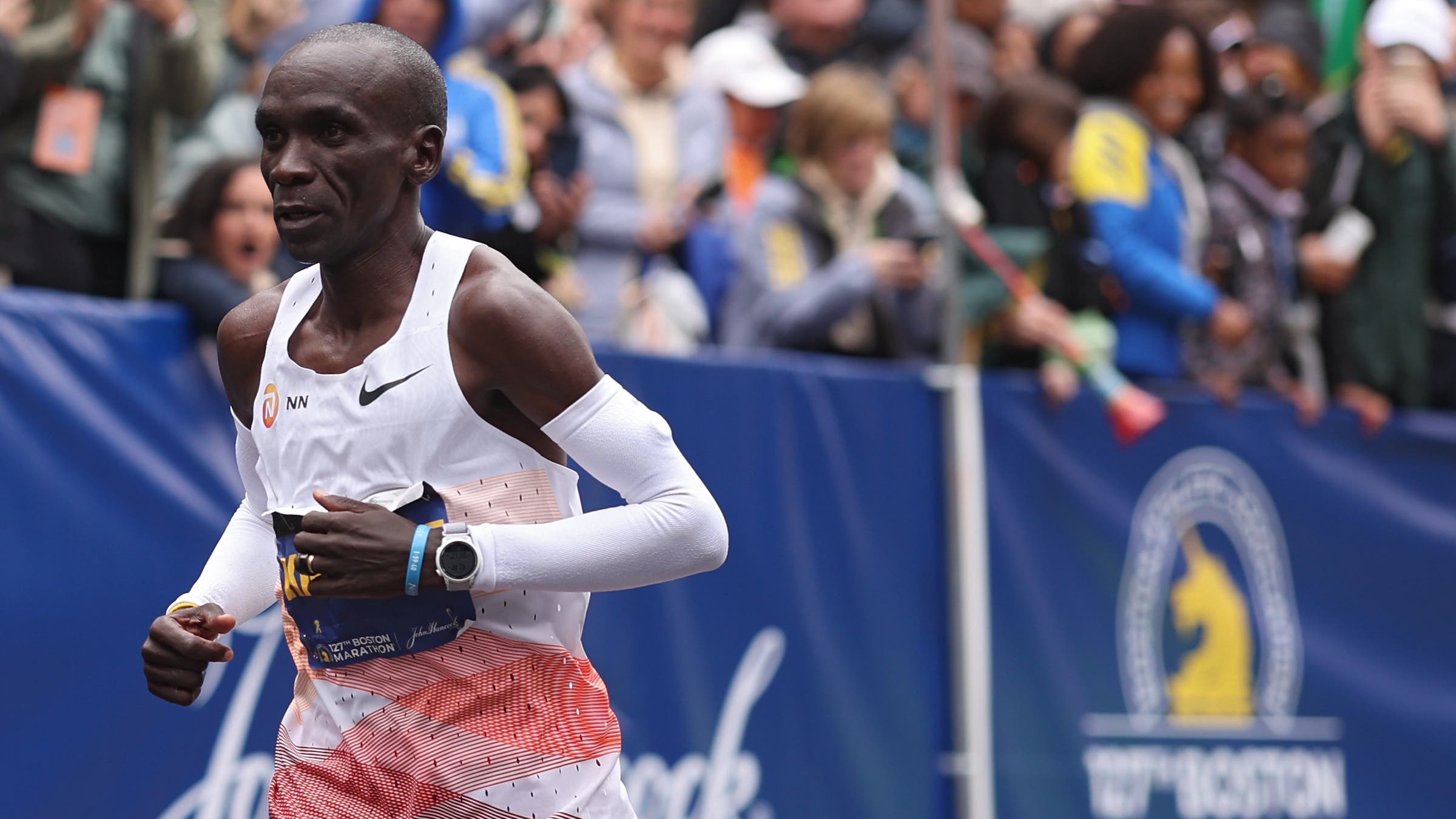 Kipchoge finishes the Boston Marathon. He wears a white singlet.