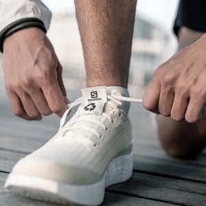 A white salomon shoe is being tied