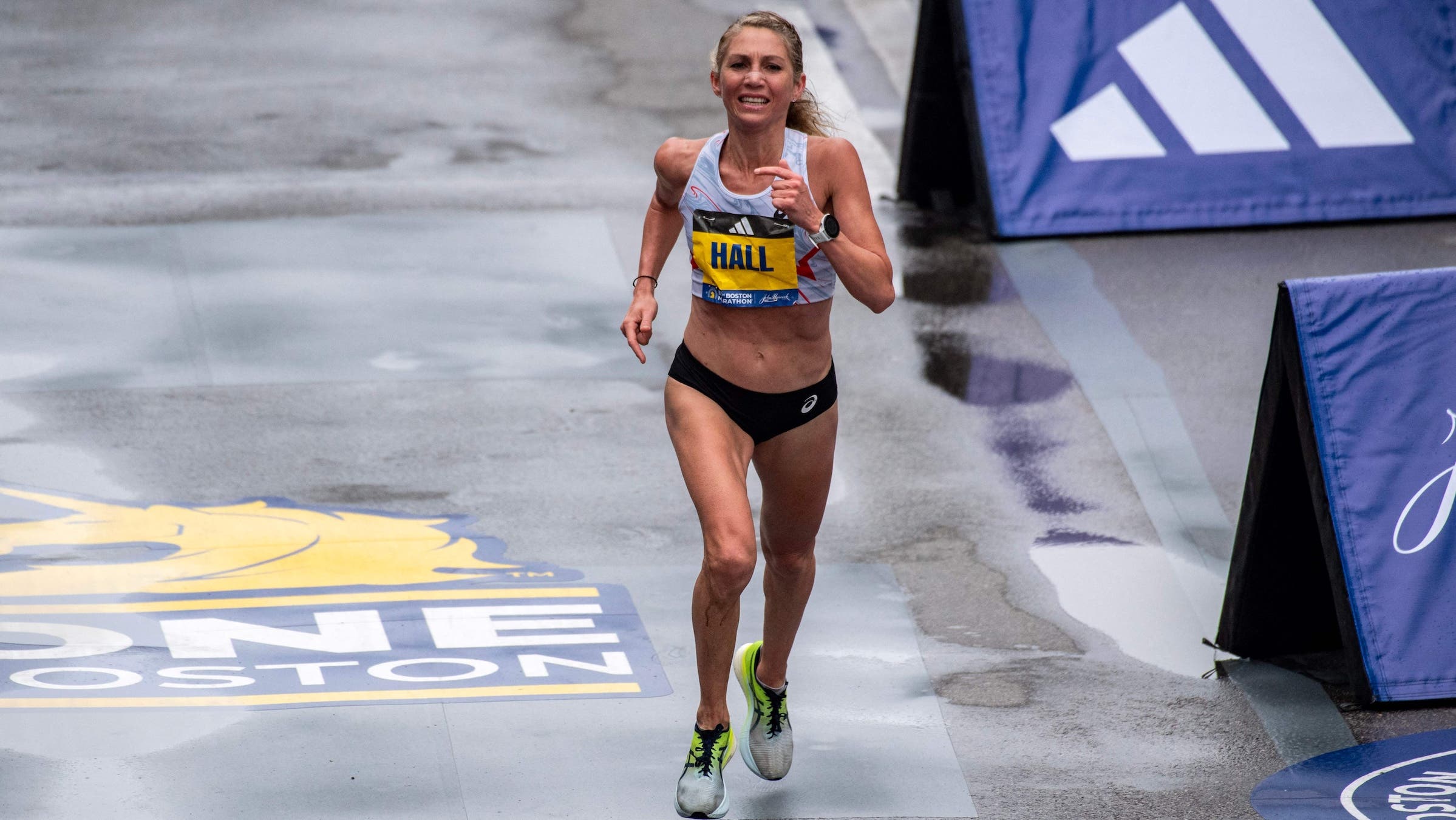 Sara Hall is wearing a white singlet and finishes the boston marathon