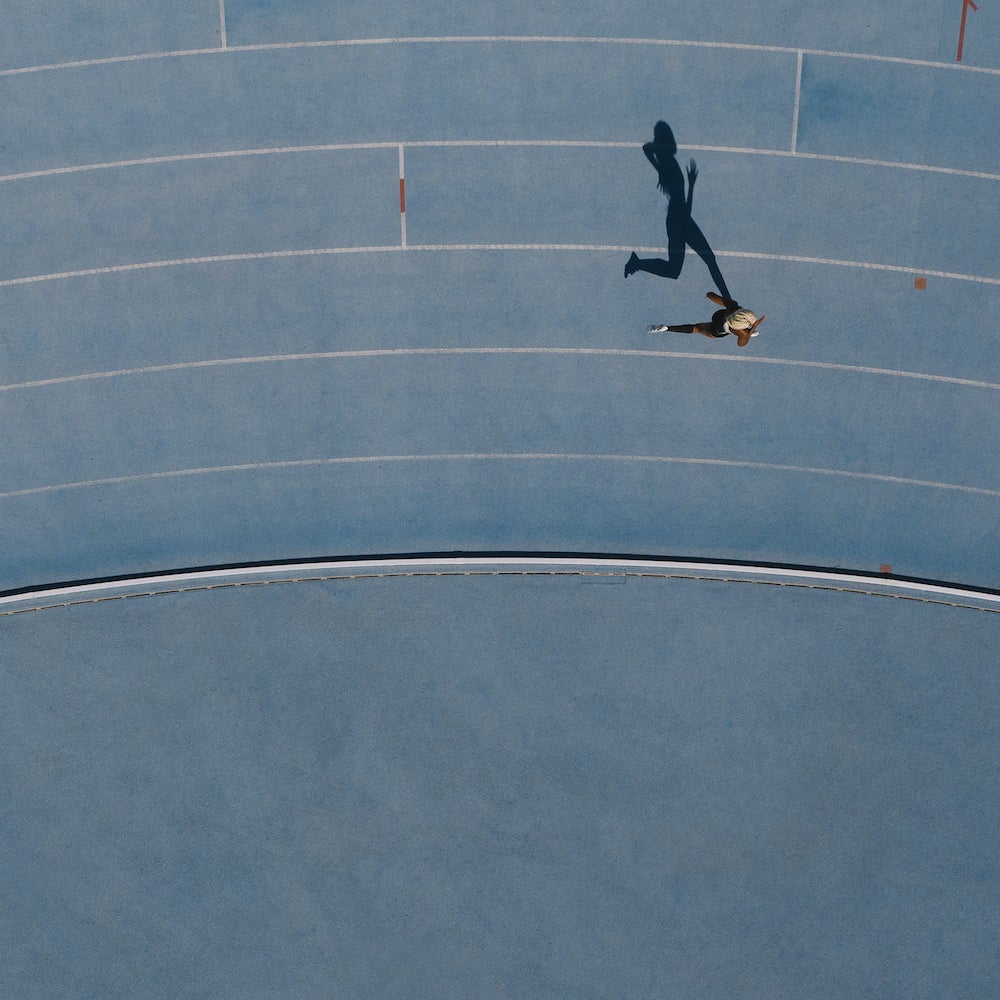 A woman runs around the bend of a light blue track, her shadow cast