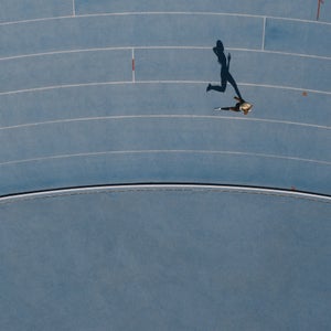 A woman runs around the bend of a light blue track, her shadow cast
