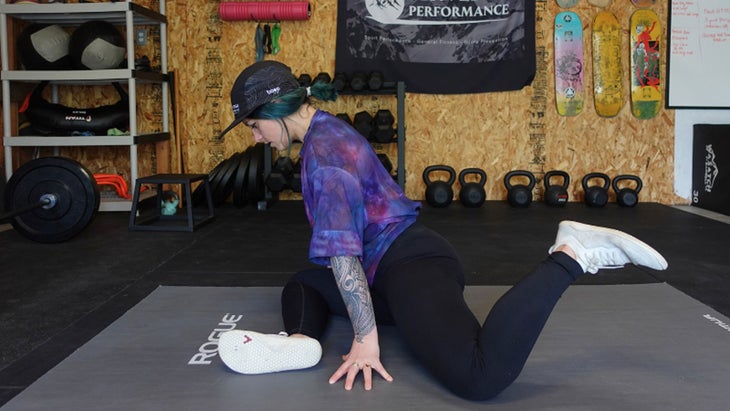 One of the mobility exercises for knee pain. A woman is in a seated position with one leg and front and one leg behind her, with both legs angled at 90 degrees. The rear foot is lifted off of the ground.
