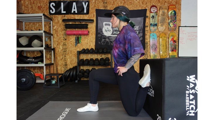 One of the mobility exercises for knee pain. A woman in a half-kneeling position bends her back leg so that her shin is parallel with a box. Her posture is upright.