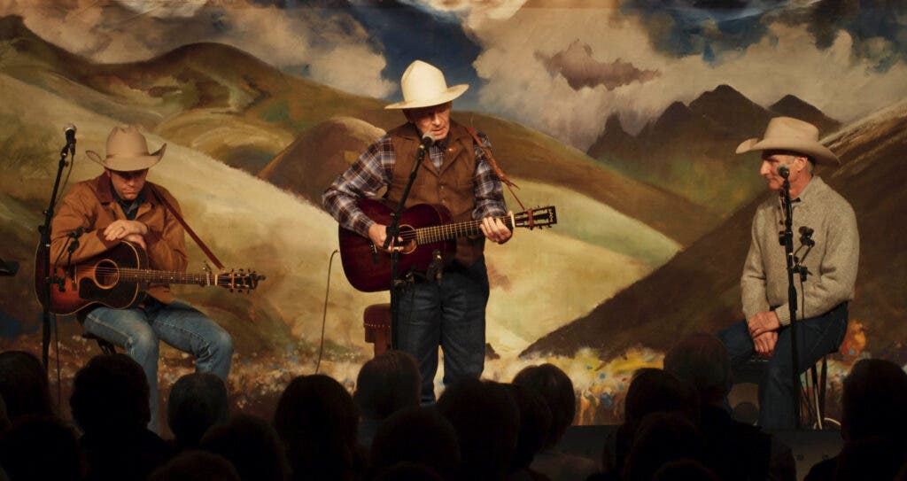 Three cowboys performing on a stage in front of a crowd. 