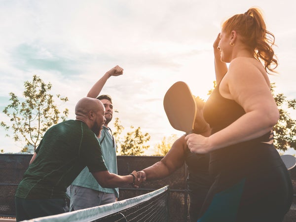 A group of adults play pickleball outside