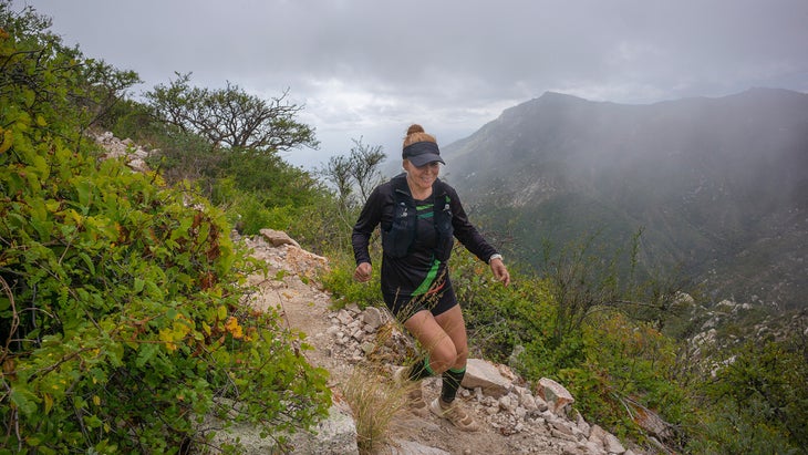 A woman runs a misty trail with rain clouds behind her