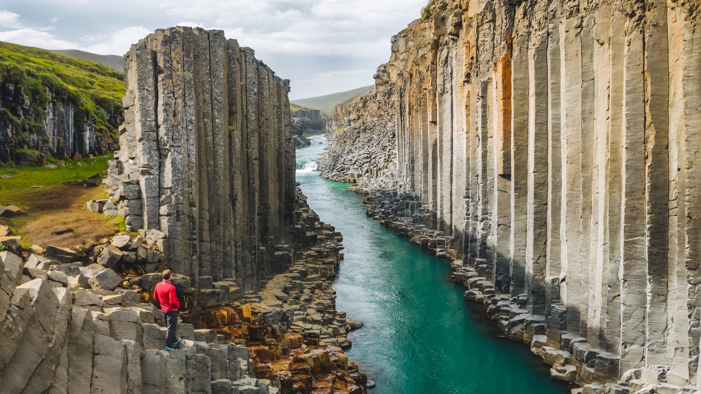 A hiker in red jacket looking down at Studlagil, a basalt canyon in Iceland