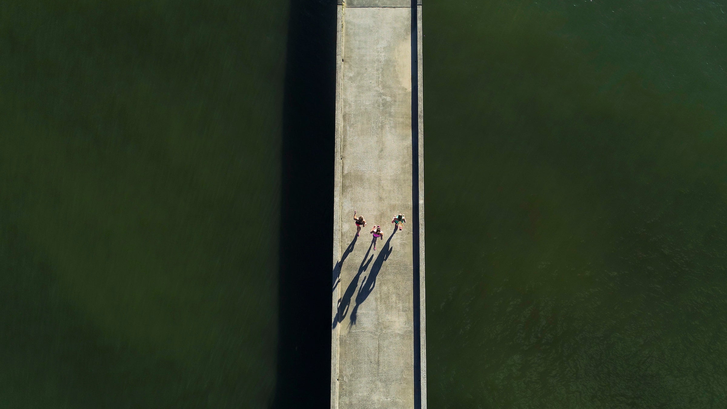Three woman run on a bridge over green water