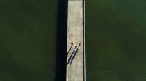 Three woman run on a bridge over green water