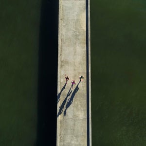 Three woman run on a bridge over green water