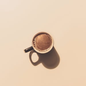 A single coffee cup with milk in the middle of a tan background