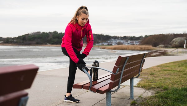 A young woman working out running in a cold day outside and stopped to stretch on a bench