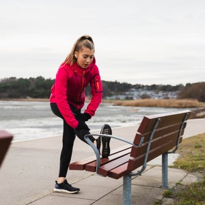 A young woman working out running in a cold day outside and stopped to stretch on a bench