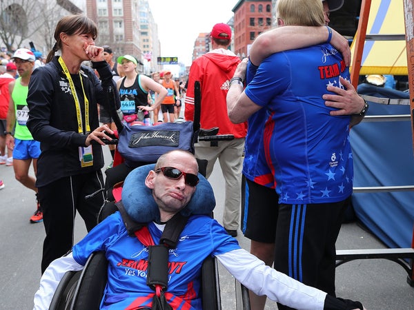 A man is assisted in a wheelchair to finish the Boston Marathon