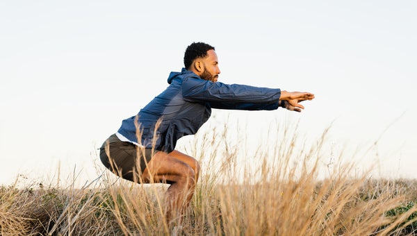Athletic male in sportswear practicing exercise and stretching agains blue sky.