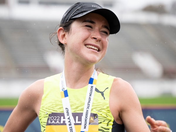 A runner in a black cap and yellow singlet finishes a race in the race, smiling.
