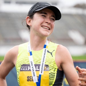 A runner in a black cap and yellow singlet finishes a race in the race, smiling.
