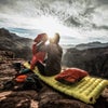 Hiker sitting on a camping pad in nature with gear surrounding them