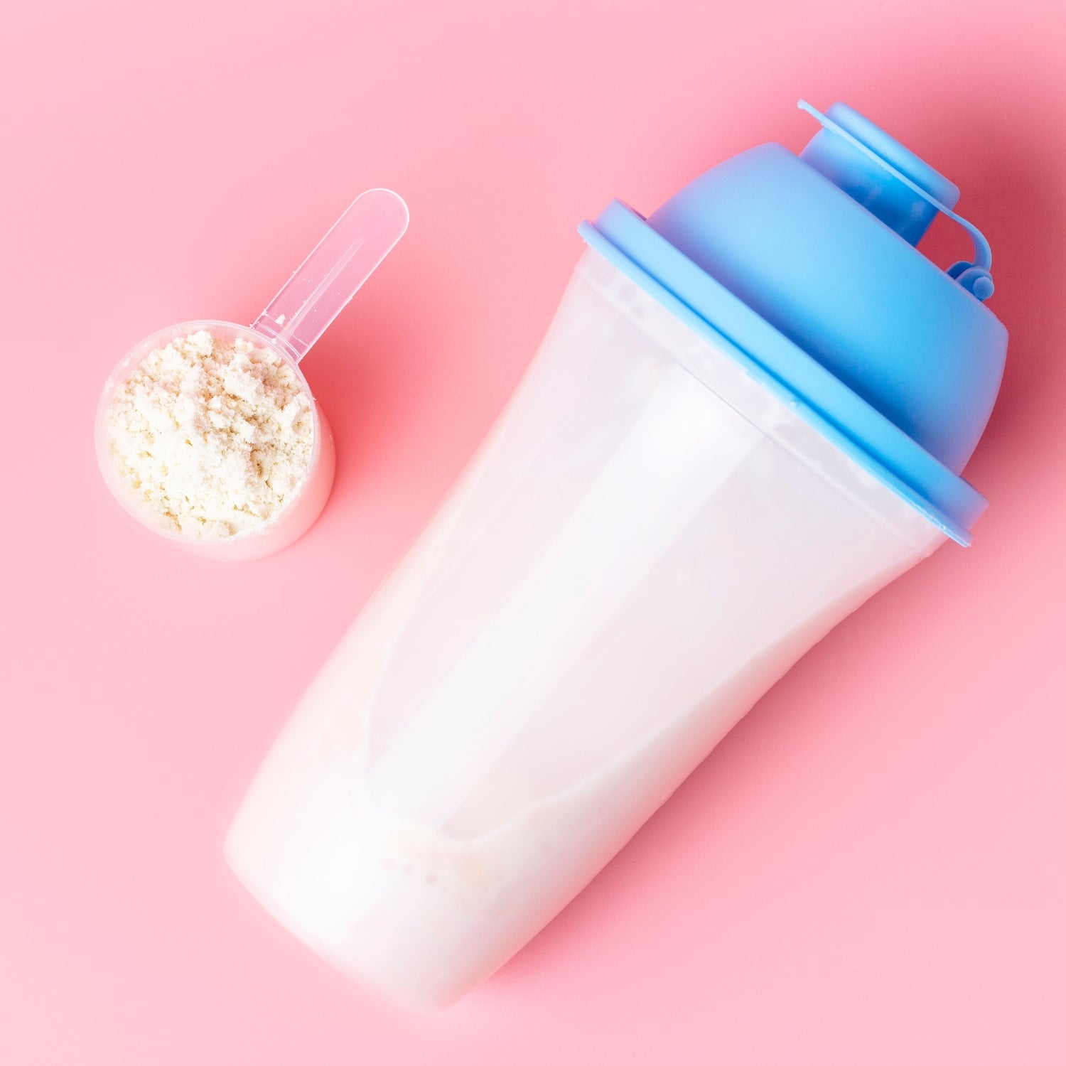 Cocktail shaker and measuring spoon with protein on pink background, top view.