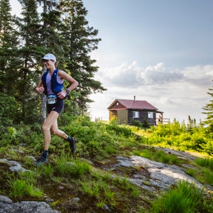 a women runs in a forest of green with a hut in the background