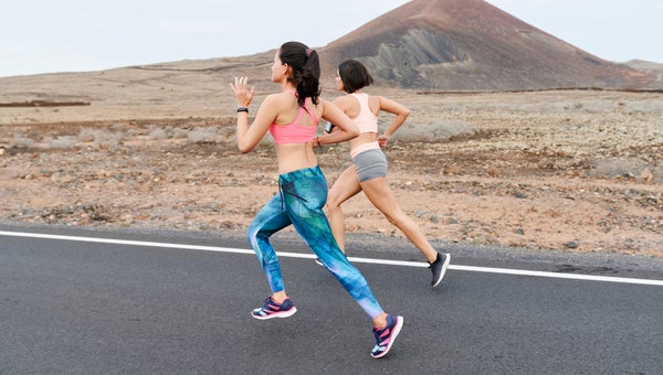 Two fit young women in sportswear running at speed along an asphalt road through rugged countryside in the summer