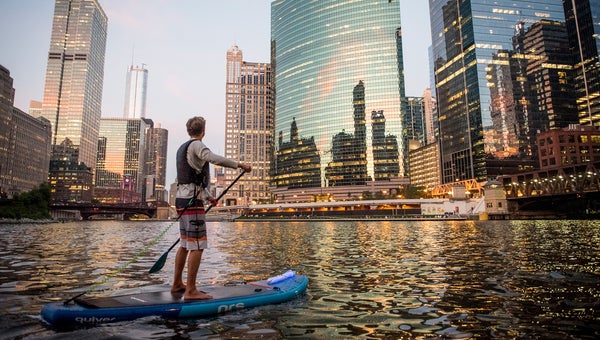 Jack Haworth paddling a standup paddleboard on the North Branch of the Chicago river at night in downtown Chicago, Illinois.