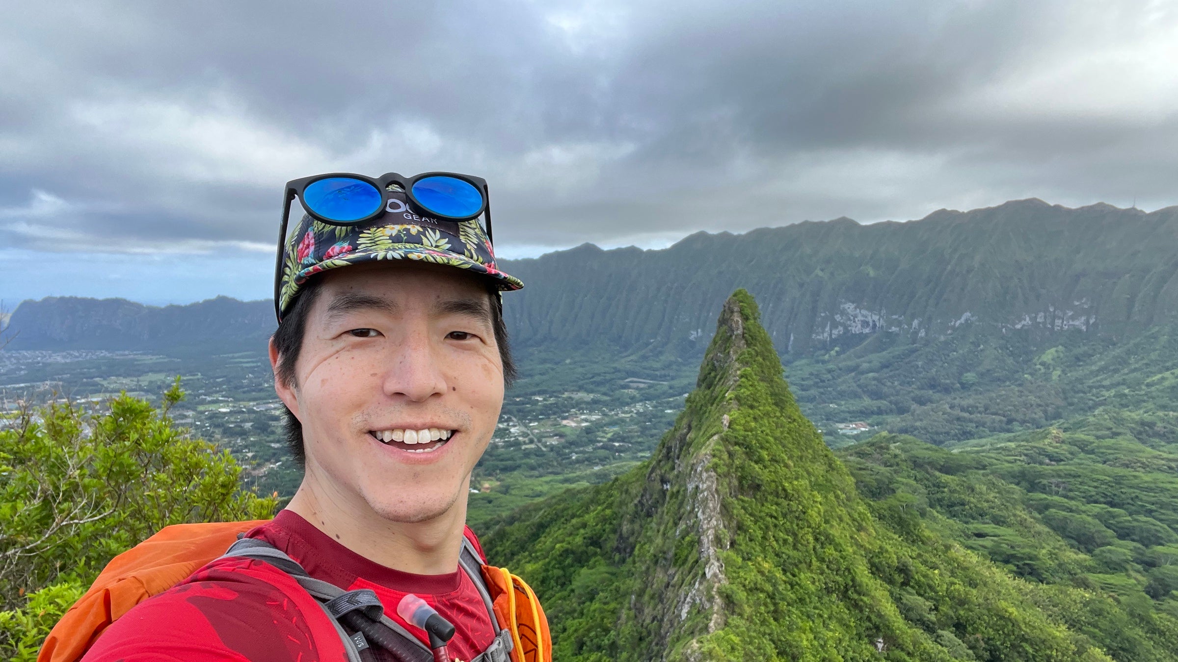 Wookie Kim in a red shirt smiling on a knife edge ridge in Hawaii