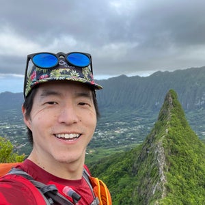 Wookie Kim in a red shirt smiling on a knife edge ridge in Hawaii