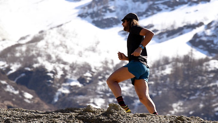 A man with long hair runs in front of big mountains