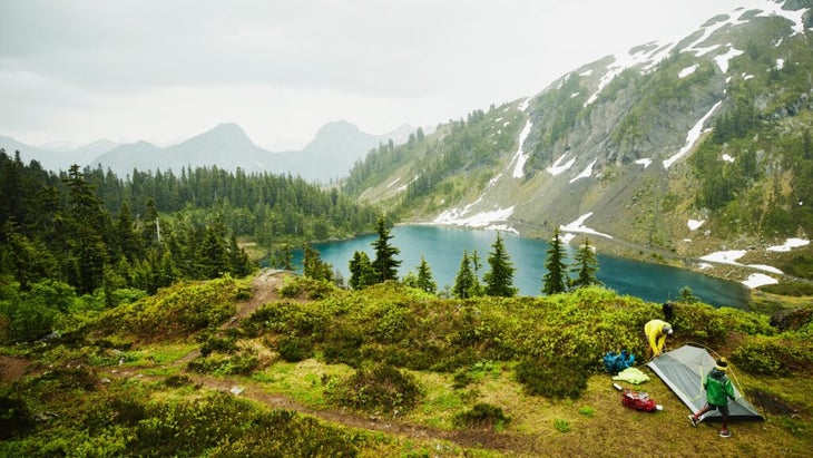 A father and his young son set a tent up overlooking a lake