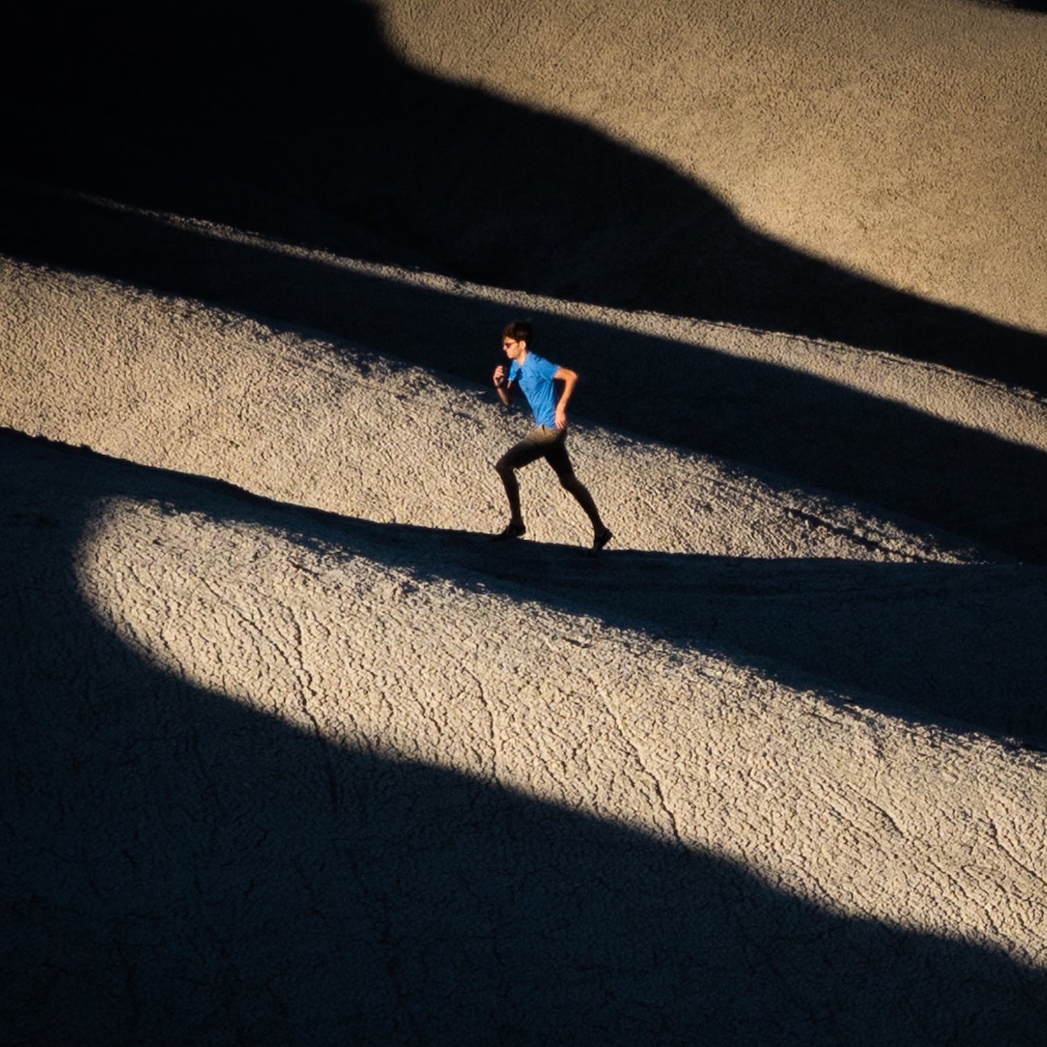A man runs up shadowy dunes