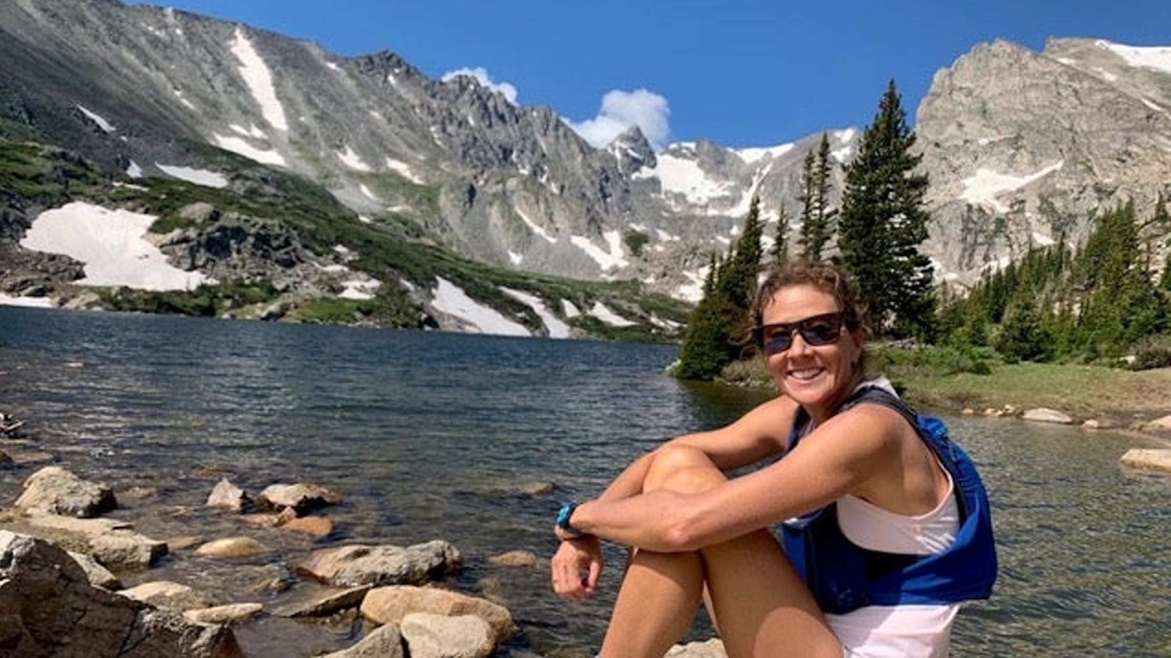 The author rests beside a high mountain lake with mountains in the background