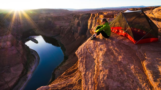 A woman sitting next to her tent overlooks the Colorado River in Arizona as the sun sets